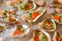 Fresh oysters served on a bed of crushed ice, each topped with a green herb mixture and a dollop of bright orange sauce.