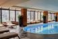 A luxurious indoor pool surrounded by lounge chairs and large windows offering a city view. 