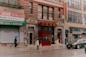 A person with an umbrella walks past closed and open shops on a rainy city street, including a restaurant with Chinese signage and a "FOR LEASE" sign in English and Chinese. A parked car and another person are also visible.