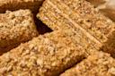 Close-up of rectangular slices of layered honey cake with a nut crumble topping and a visible creamy filling between layers, drizzled with honey.