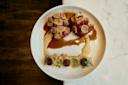 A gourmet dish on a white plate, featuring two meat portions topped with slices, drizzled with two sauces. Accompanied by a rectangular layer garnished with small mushrooms and herbs, placed on a marble surface.