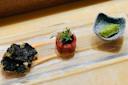 A glass plate with three items: a crispy seaweed snack on the left, a round portion of seasoned tuna tartare topped with microgreens in the center, and a small ceramic bowl holding a scoop of wasabi on the right.