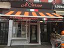 A storefront of Il Carino Restaurant with a brown and orange striped awning, Italian flag, and "Fine Italian Dining" written above the entrance. The door is flanked by windows and a small pumpkin sits outside.
