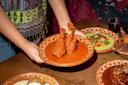 Saavedra holds a traditional clay plate with two chicken drumsticks covered in red mole sauce. Other colorful Mexican dishes are on the wooden table. 