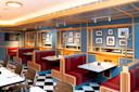 A retro-style diner featuring red booth seating and blue walls adorned with framed photos. The floor has a black and white checkered pattern. White tables are set with condiments, and the space is lit with overhead lighting.