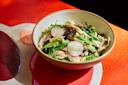 A bowl of mixed green salad with shredded chicken, sliced radishes, and green beans sits on a colorful red and beige table.