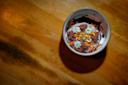 A ceramic bowl filled with a chocolate dessert garnished with nuts, edible flowers, and green herbs, placed on a wooden surface with warm lighting casting a shadow.