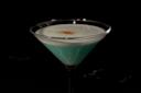 A blue cocktail in a martini glass, topped with a layer of white foam and a sprinkle of brown garnish, set against a dark background.