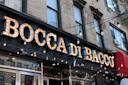 The exterior of a restaurant named Bocca di Bacco, featuring a large, illuminated sign. The building has several windows and a string of hanging lights.