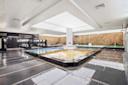 A spacious indoor spa with multiple rectangular pools, modern black and white decor, stone accent walls, and large ceiling lights reflecting on the wet tiled floor.