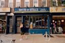 A person walks past the storefront of “Sotto le Stelle,” a pizzeria and paninoteca on a city street, with brick buildings and other shops visible on either side.