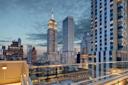 Rooftop view of midtown Manhattan at dusk, featuring the Empire State Building and surrounding skyscrapers under a partly cloudy sky, with glass railings in the foreground.