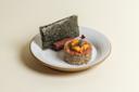 A plated dish featuring a round serving of rice topped with orange sea urchin and garnish, accompanied by a rectangular cracker and a sheet of nori, served on a white plate with a tan rim.