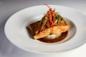 Grilled salmon fillet served on a bed of rice, topped with julienned vegetables, and surrounded by a brown sauce on a white plate.
