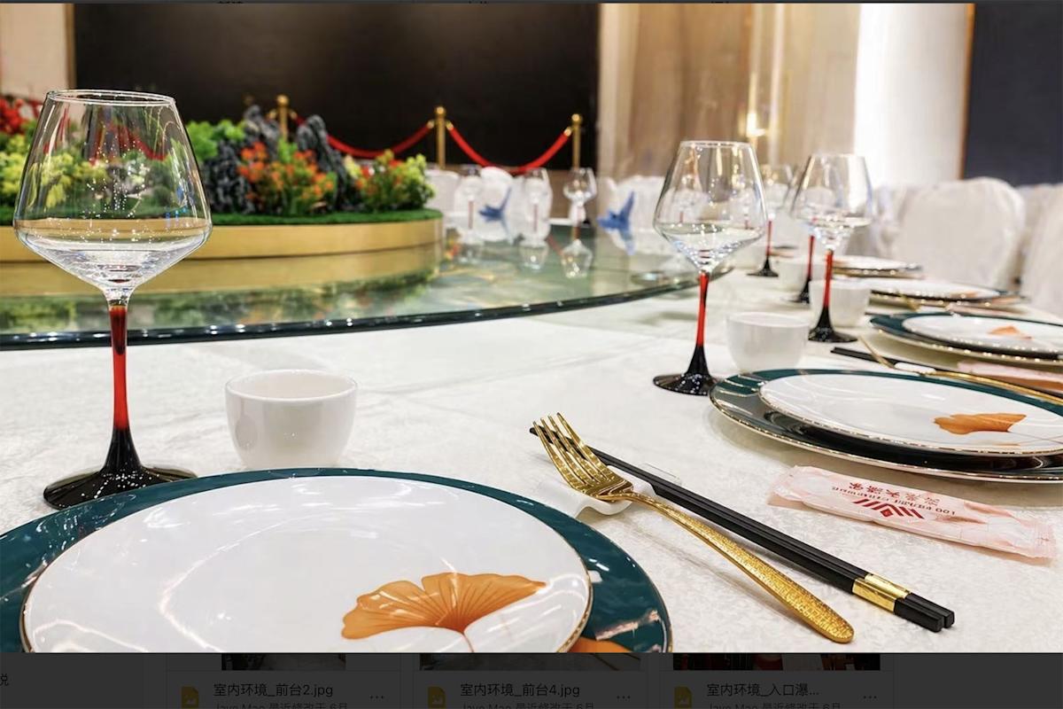Elegant dining table set with plates, gold utensils, chopsticks, wine glasses, and a centerpiece of fruit. The table has a decorative green and gold theme with a rotating tray in the center.