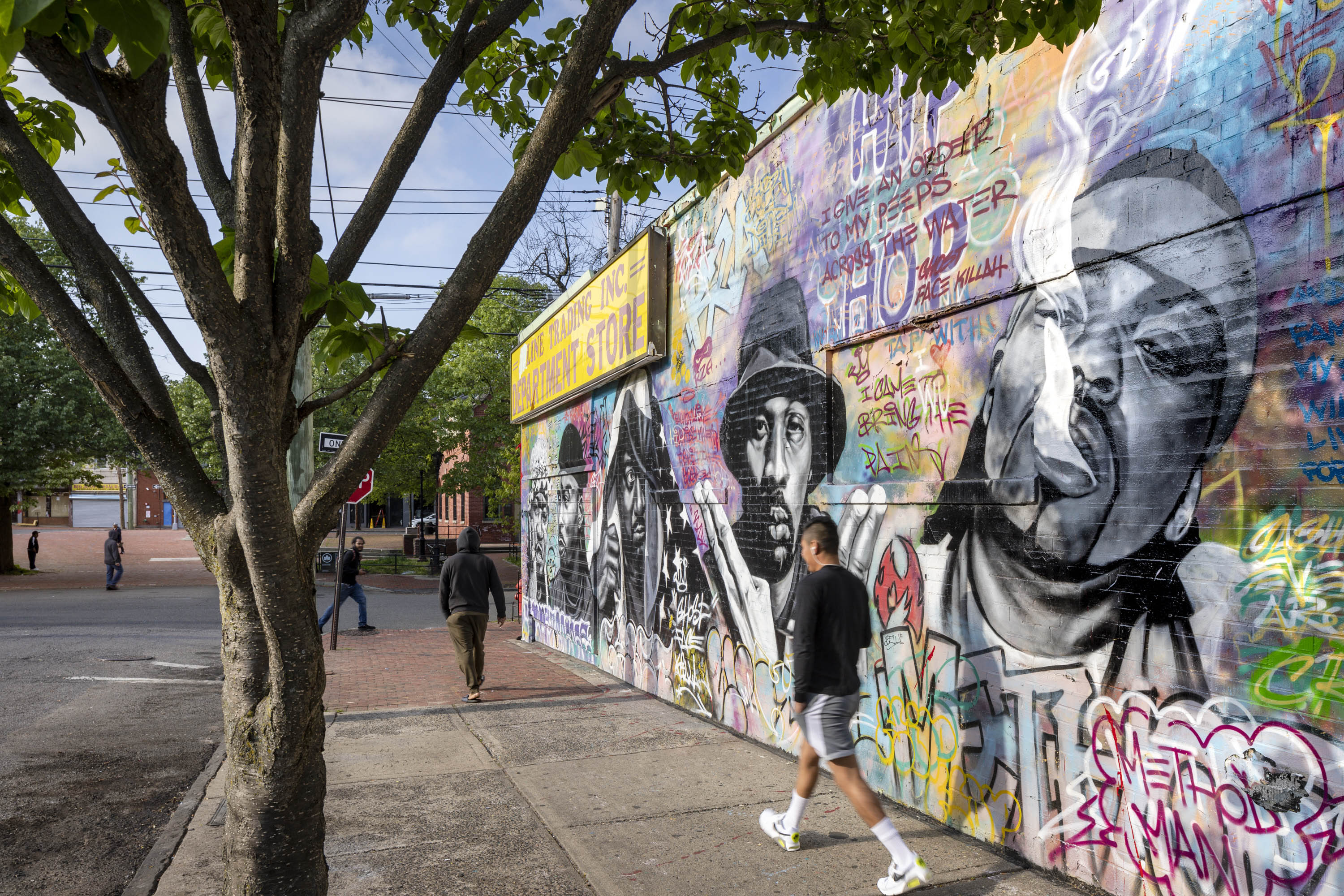 People walking next to Wu Tang Clan Mural on wall of the side of the street