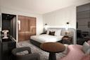 Modern hotel room with a large bed, side tables, contemporary lighting, a round wooden table, upholstered chairs, a TV, a marble desk, and a wardrobe with glass doors. The decor features neutral tones and sleek finishes.