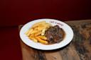 A white plate labeled "Café d'Anvers" holds a serving of golden French fries and a portion of beef stew with dark gravy, set on a rustic wooden table with a red background.