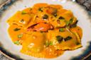 A plate of ravioli in a creamy orange sauce, garnished with fresh herbs and diced green vegetables, with a piece of lobster claw placed on top.