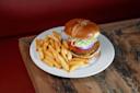A plate with a cheeseburger topped with lettuce, tomato, and red onion on a brioche bun, served with a side of golden French fries on a rustic wooden table.