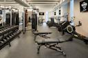 A spacious, modern gym with various exercise equipment including treadmills, exercise bikes, weight machines, dumbbells, and benches. The gym has bright lighting and a clean, organized layout with Hard Rock branding on the walls.