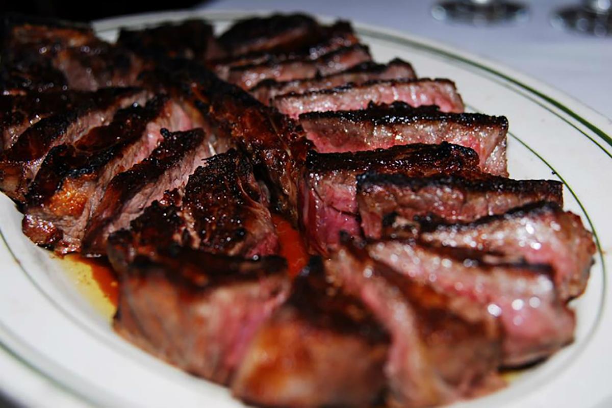 Sliced, juicy steak arranged on a white oval plate with a green trim, showing a seared, charred exterior and pink, tender center.