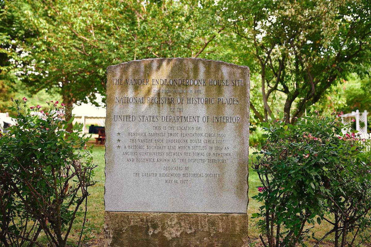 A stone marker among trees and bushes commemorates the Vander Ende-Onderdonk House Site; it details its historical significance and mentions the United States Department of Interior.