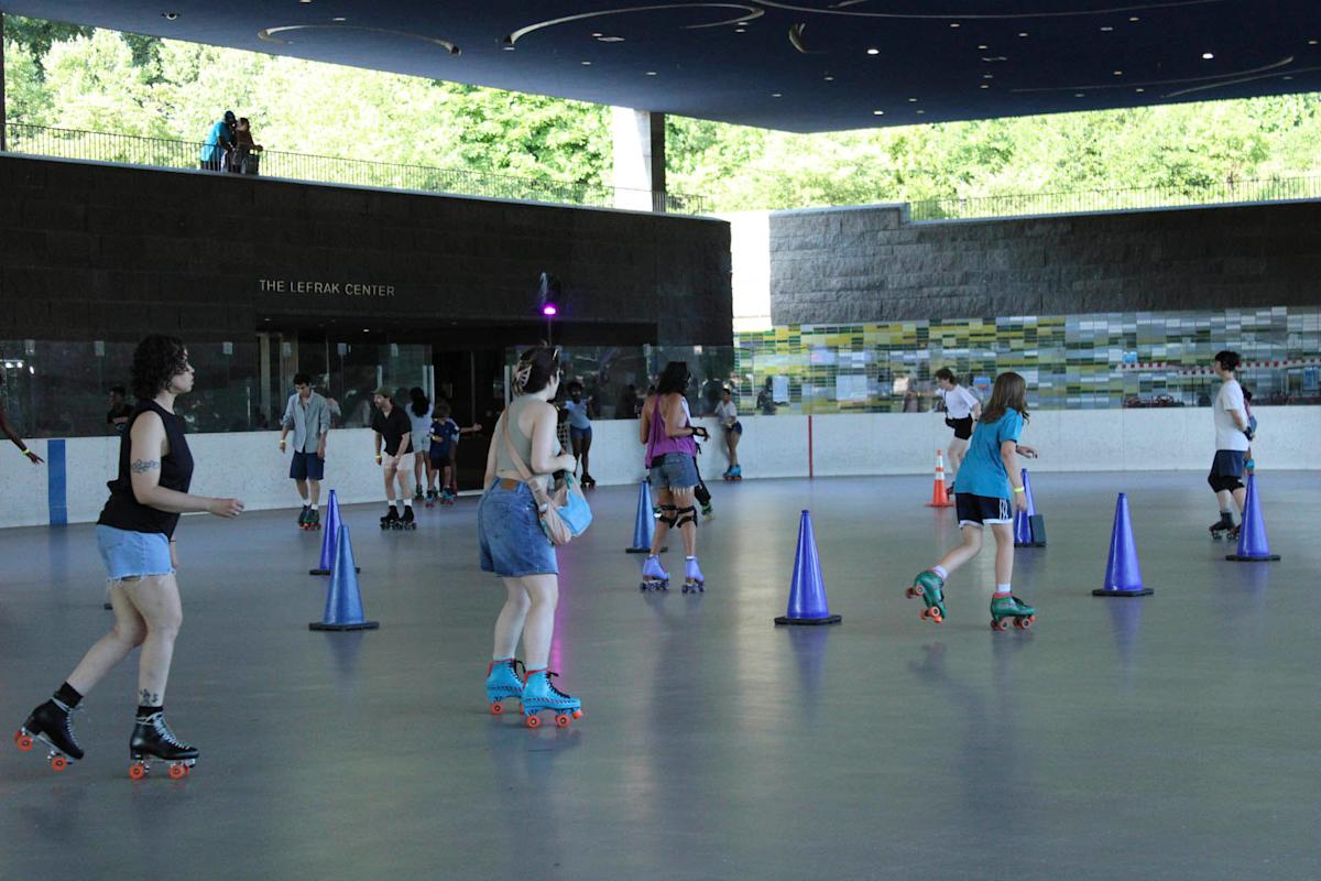 People roller skating around purple cones inside a rink at the LeFrak Center. The setting is bright with natural light coming through large windows. Skaters are dressed casually, and the indoor space has a modern design.