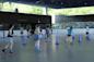 People roller skating around purple cones inside a rink at the LeFrak Center. The setting is bright with natural light coming through large windows. Skaters are dressed casually, and the indoor space has a modern design.