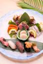 A colorful plate of assorted sushi and sashimi, including slices of salmon, tuna, scallops, white fish, lemon wedges, sea urchin, and garnishes, arranged artfully on a round dish with a green leaf.