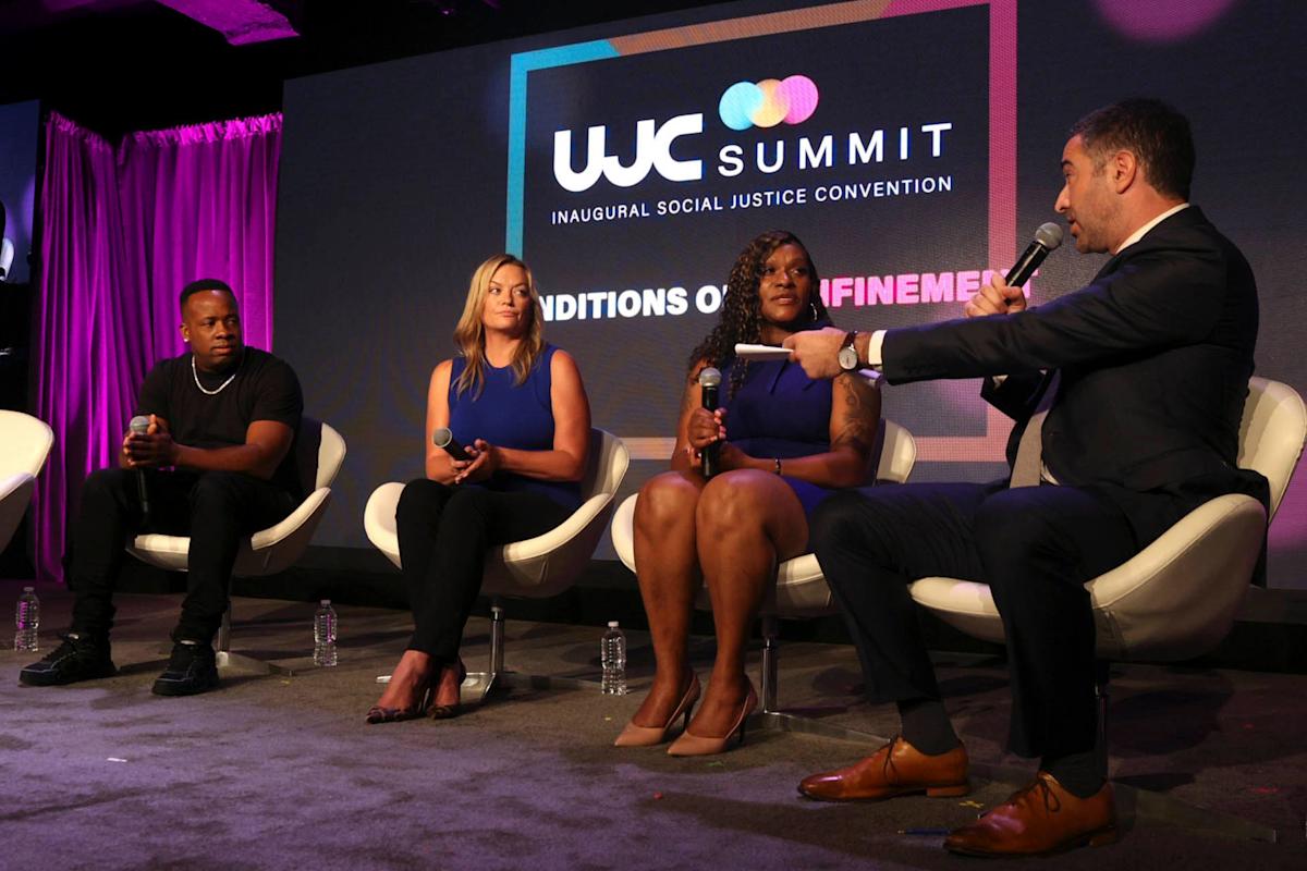 Four panelists sit on stage in modern white chairs at the WJC Summit, participating in a discussion. Three people are listening as one man speaks into a microphone. A WJC Summit sign is visible in the background.