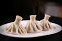 Three steamed dumplings on a white plate, with crimped tops and sprinkled with black pepper, set against a dark background.