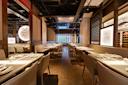 Modern, upscale restaurant interior with neatly set tables, beige chairs, elegant lighting, decorative wall features, and a wine display, creating a warm and inviting dining atmosphere.