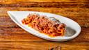 A serving of rigatoni pasta with rich meat sauce and grated cheese is arranged neatly on a white, leaf-shaped plate, set on a rustic wooden table.