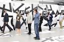 A group of people wearing virtual reality headsets walk and stand in a modern room with abstract black and white geometric patterns on the walls and floor.