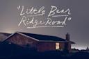 A house with a dark roof and a single lit window is seen at dusk, with the handwritten words "Little Bear Ridge Road" in white above it against a gray-blue sky.