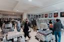 A sports memorabilia store with several people browsing. Shelves are filled with trading card boxes, and framed jerseys hang on the walls. The store sign reads "Dave & Adam's New York City.