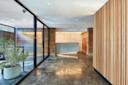 A modern office lobby with polished concrete floors, wooden slat walls, glass partitions, a large potted plant, and a geometric reception desk under contemporary lighting.