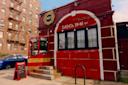 A red brick restaurant called Jack’s with large front windows, a wooden entryway, and a sandwich board menu on the sidewalk. An apartment building and a blue car are visible in the background.