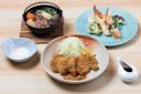A Japanese meal featuring fried cutlets with shredded cabbage and lemon, a bowl of sukiyaki with vegetables and beef, assorted tempura on a blue plate, a small bowl of dipping sauce, and a sauce pitcher.