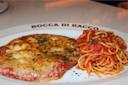 A plate with breaded veal cutlet topped with melted cheese and herbs, next to spaghetti in tomato sauce with herbs. The plate is labeled "Bocca di Bacco.