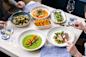 A table set for two with elegant dishes, including scallops on green sauce, fish with asparagus, a plate of asparagus and peas, a curry with bay scallops, and a dish of breaded sticks. Two glasses of wine and a blue napkin complete the setting.