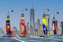 Four colorful sailboats from Spain, Great Britain, Brazil, and the USA race on the water with the New York City skyline and One World Trade Center in the background. Speed indicators appear above each boat.