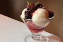 A glass dessert cup with scoops of white and red sorbet, topped with fresh blackberries and a small mint sprig, sits on a white tablecloth.