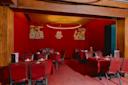 A dimly lit restaurant with red walls and tablecloths, set with plates and chopsticks. Decorative Chinese dragon and phoenix wall art, along with a circular light fixture, hang above the tables.