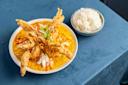 A bowl of seafood curry topped with fried soft-shell crab, garnished with herbs and red pepper strips, sits on a blue tablecloth. A small bowl of white rice accompanies the dish.