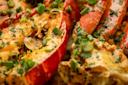 Close-up of a cooked lobster dish topped with melted cheese, chopped green onions, and herbs, highlighting the vibrant reds of the lobster shell and the fresh green garnishes.