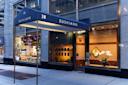 The exterior of Sushiann restaurant at 38, featuring a dark blue awning, large glass windows, modern decor, and a display of white orchids in the entrance area.