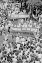 Black-and-white photo of a large crowd at a street protest. People hold banners reading “NY NETWORK” and “Fighting For Our Lives,” surrounded by onlookers, some of whom are clapping and wearing t-shirts.