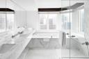 Modern bathroom with marble countertops, double sinks, a glass shower, and a bathtub by large windows overlooking a cityscape. White walls and natural light create a bright, spacious atmosphere.